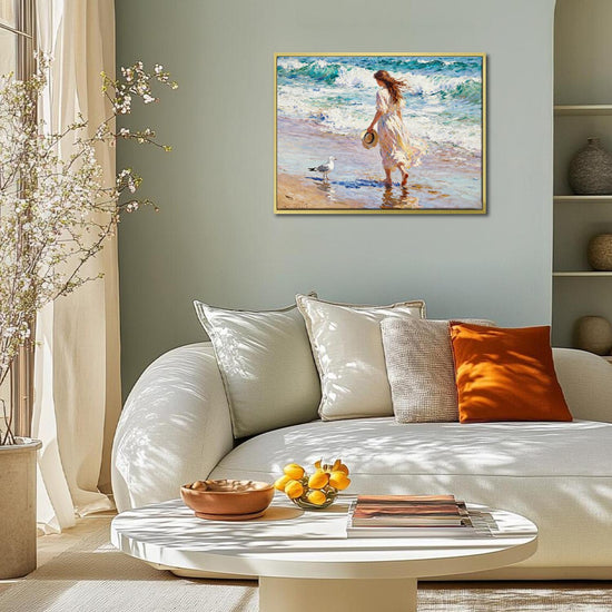 gold frame wall art painting depicts a woman in a flowing long dress walking on the beach, accompanied by seagulls.