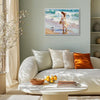 white frame wall art painting depicts a woman in a flowing long dress walking on the beach, accompanied by seagulls.
